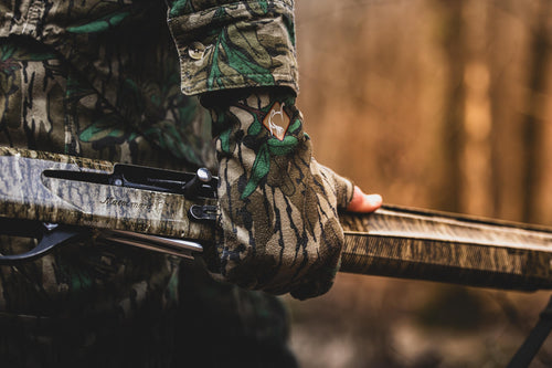 Performance Stretch-Fit Shooter Turkey Gloves, showcasing silicone grip texture, held by a camouflaged person, emphasizing their utility in outdoor hunting activities.