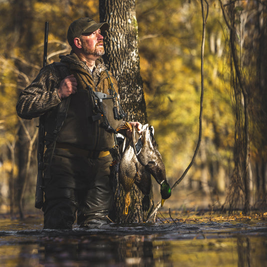 Hunter in marsh, wearing MST Endurance Quarter Zip Jacket with Hood, holding ducks and shotgun. Emphasizes mobility and breathability for outdoor pursuits.