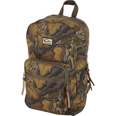 The Waterfowl Throwback 80 Backpack in Mossy Oak Fall Foliage features a leaf-patterned cotton canvas, multiple zip pockets, brown pulls, top handle, and a front brand patch.