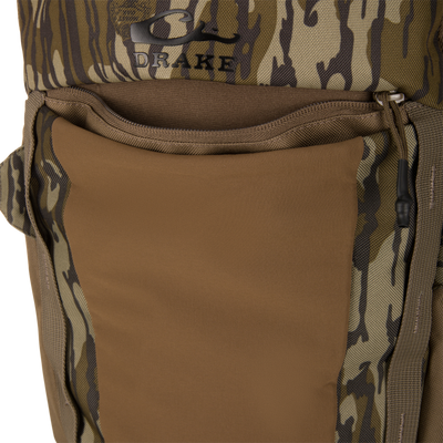 Drake Campus Backpack close-up showing camo fabric, zippered pocket, padded panel, and Drake logo, highlighting its durability and organization for versatile outdoor use.