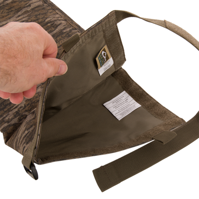 The Migrator Gun Case opened, revealing an empty olive-green interior, camo-patterned exterior, and webbing shoulder strap, emphasizing its durable, waterproof design for professional gear protection.