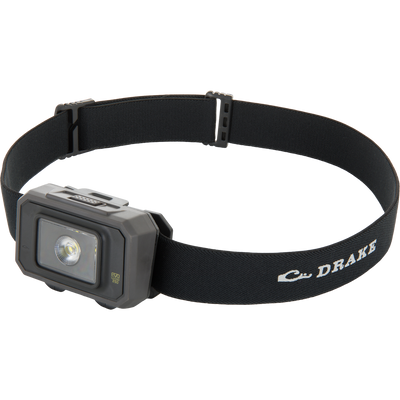 The Waterfowl 3 Headlamp Lighting Pack 250LM is a black adjustable dual-fuel headlamp with a rectangular 250 lumen LED and DRAKE printed on the elastic strap—an affordable adventure lighting kit.