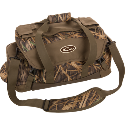 The Waterfowl Large Blind Bag in Mossy Oak Original Shadow Grass features multiple pockets, tan and shoulder straps, a front oval CW logo, and is made from heavy-duty nylon for durability.