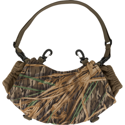 The Waterfowl LST Handwarmer Muff features a camouflage pattern, shoulder strap, waterproof cell phone pocket, and two black clips for outdoor or hunting use, shown on a white background.