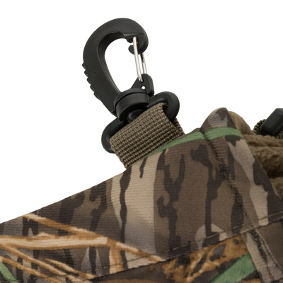 Close-up of a camouflage-patterned fabric with a black plastic clasp on a green strap, part of the Waterfowl LST Handwarmer Muff, shown against a white background.