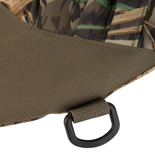 Close-up of camouflage fabric and olive green textured material joined at a seam on a Waterfowl LST Handwarmer Muff, featuring a black plastic D-ring and fabric loop near the bottom edge.