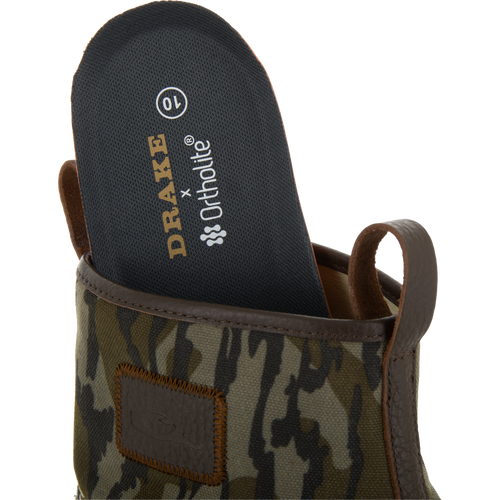 Close-up of a camouflage-patterned Drake x Ortholite insole being placed into the Throwback 80 Waxed Canvas Slip On Duck Boot, highlighting its removable feature.