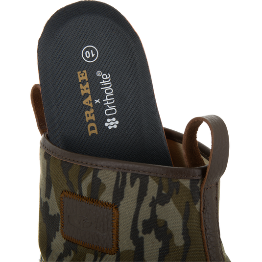 Close-up of a camouflage-patterned Drake x Ortholite insole being placed into the Throwback 80 Waxed Canvas Slip On Duck Boot, highlighting its removable feature.