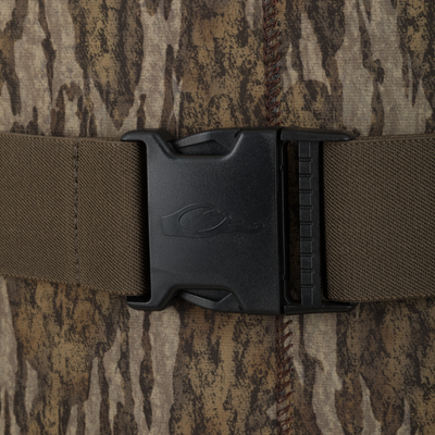 Close-up of a black plastic buckle fastened on an adjustable strap of the Waterfowl Youth Neoprene Wader, against brown and tan camouflage fabric with visible stitching.