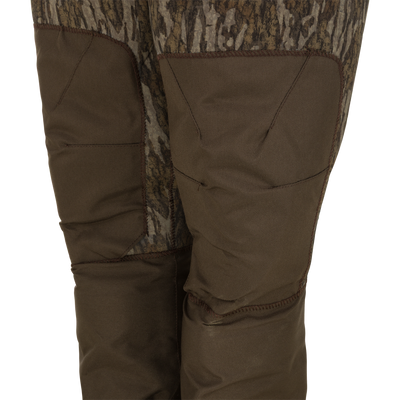 Close-up of the Waterfowl Youth Neoprene Wader featuring a camouflage pattern, reinforced brown knee patches, and an adjustable belt—ideal for outdoor or hunting use.