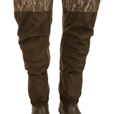 Hardline Breathable Youth Wader with camo thighs, reinforced knees, elastic ankles, and molded rubber boots on a display stand, designed for young outdoor enthusiasts.