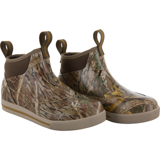 The Camp Deck Boot by Waterfowl features a Mossy Oak Shadow Branch camo pattern, waterproof neoprene construction, ankle-high design, and looped pull tabs at the back.