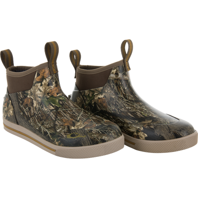 The Waterfowl Camp Deck Boot features an ankle-high, waterproof design with Mossy Oak Original Break Up camo, brown pull tabs, and tan rubber soles—perfect for outdoor use.