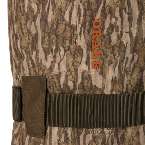 Close-up of Hardline Insulated Breathable Wader, showcasing camo fabric, adjustable strap with buckle, and orange DRAKE logo, highlighting durable, waterproof, insulated features.
