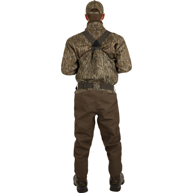 A man wearing the Insulated Guardian Elite HND Front Zip Wader with camouflage jacket and hat, showcasing durable, waterproof hunting gear with Thinsulate® boot lining.