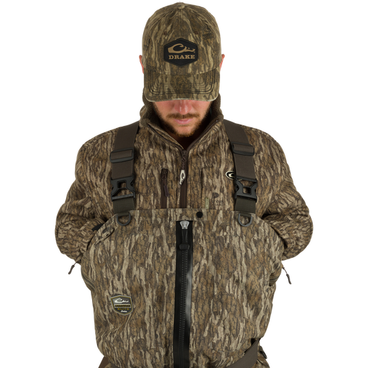 Man wearing Insulated Guardian Elite HND Front Zip Wader, featuring a camouflage jacket and hat, designed for warmth, durability, and waterproof protection.
