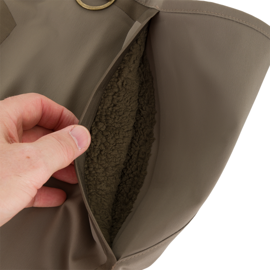 A hand opens a fleece-lined chest pocket on these brown Drake X Ducks Unlimited BMF1600 Kevlar Wader waterproof hunting waders.