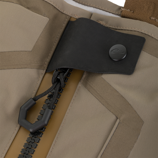 Close-up of a tan Drake X Ducks Unlimited BMF1600 Kevlar Wader chest featuring a heavy-duty front zipper with a rubberized pull tab and a protective flap secured by a snap button.