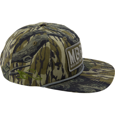 A camouflage Drake x Lost Hat MBRGA Patch Goat Rope Cap by Waterfowl with a flat brim, large MBG patch, green fish embroidery on the side, and an easy snap back closure.