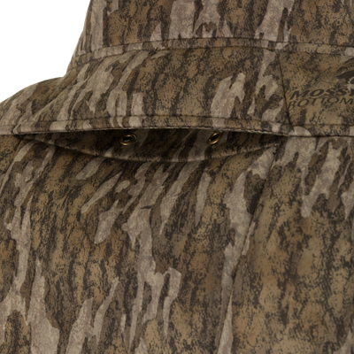 Close-up of a camouflage-patterned Non-Typical Midweight Nova Silencer Jacket with Scent Control by Nontypical, featuring visible stitching, metal grommets, and a partial MOSSY OAK BOTTOMLAND logo.