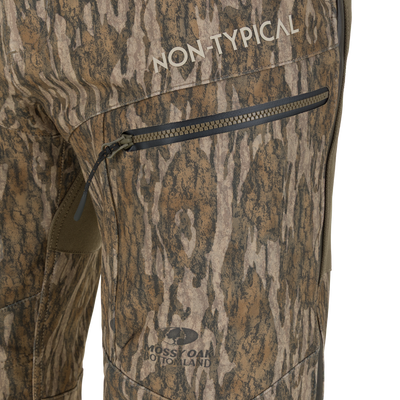Close-up of Non-Typical Pursuit Softshell Pant with Agion Active X2 windproof hunting pants in camouflage, featuring a zippered thigh pocket, the text NON-TYPICAL, and a MOSSY OAK BOTTOMLAND logo.