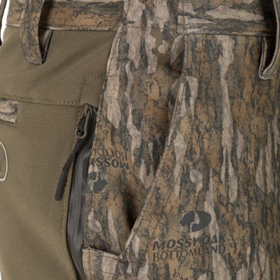 Close-up of olive green and camouflage Non-Typical Pursuit Softshell Pant with Agion Active X2 hunting pants featuring a side zipper pocket and printed Mossy Oak Bottomland branding.