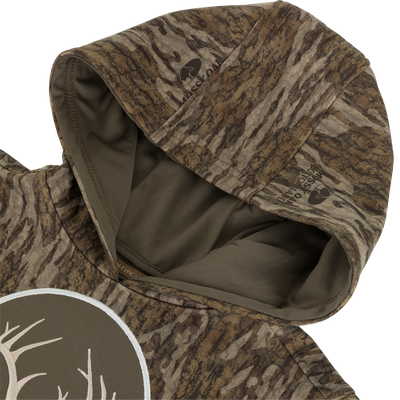 A close-up of the Non-Typical Youth Performance Hoodie with Agion Active X2 by Nontypical, showing a brown and green camo pattern, partial deer antler graphic, tree-bark textures, and anti-odor technology.