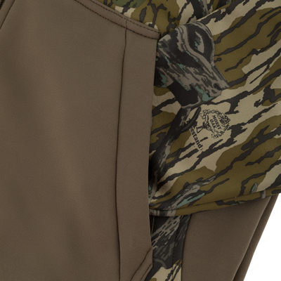 Close-up of a zippered pocket on a Nontypical Youth Endurance Full Zip Jacket with Hood, featuring a solid olive panel and a camouflage pattern with a Mossy Oak logo.