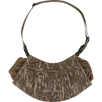 The Non-Typical Handwarmer Muff with Scent Control by Nontypical features a camo pattern, zippered front pocket, adjustable brown strap with black buckles, scent control tech, and a white Non-Typical circular logo on the front.