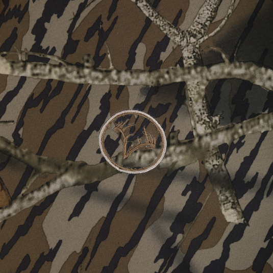 The Nontypical Non-Typical Slacker Quarter Zip Hoodie features brown and green camo with realistic branches and an embroidered circular deer silhouette patch at the center.