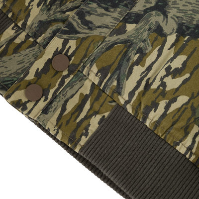 Close-up of the Campfire Canvas Bomber Jacket by Lifestyle in a camo pattern, with two brown buttons, a ribbed dark green hem, and fabric featuring green, brown, and beige abstract shapes.