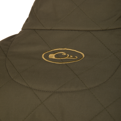 Close-up of the olive green quilted fabric on the Lifestyle Delta Quilted Jacket, showing a yellow embroidered oval logo with a stylized duck head at its center.