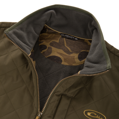 Close-up of the Delta Quilted Jacket by Lifestyle: olive green with a fleece-lined collar, camouflage inner lining, and gold embroidered chest logo—perfect for outdoor performance.