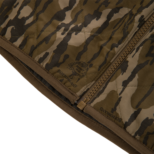 Close-up of a Lifestyle Delta Quilted Vest in a green and brown camouflage print, featuring a front zipper and a Mossy Oak Bottomland logo.