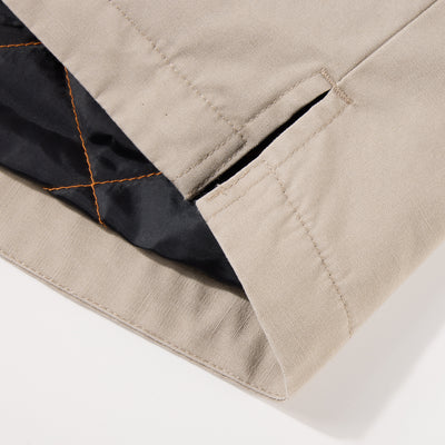 Close-up of Campfire Canvas Shirt Jac Hoodie's hem, showing beige canvas fabric, reinforced slit, and quilted black lining with orange stitching for warmth.