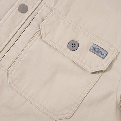 Close-up of the Drake Campfire Canvas Shirt Jac Hoodie, highlighting a flap-style chest pocket with a button, top-stitching, and a fabric logo tag.