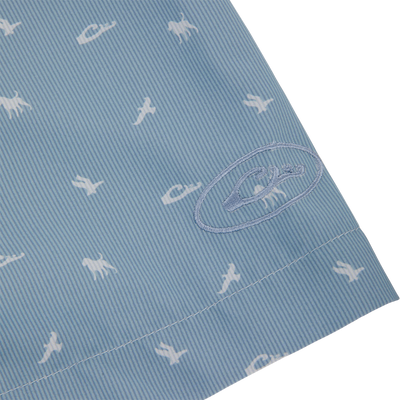 Close-up of the Cinco Ranch Western Short Sleeve Shirt featuring light-blue seersucker fabric with white prehistoric creature silhouettes and an embroidered logo on the hem.