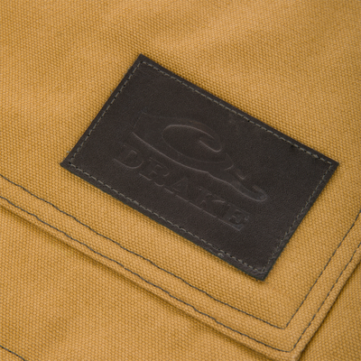A rectangular brown leather patch with a debossed duck logo and the text DRAKE sewn onto the tan canvas of a Lifestyle Canvas Sherpa Lined Work Vest.