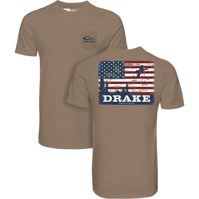 The Lifestyle Americana Scenic Flag T-Shirt in Savanna Tan features a small Drake logo on the pocket and a large American flag, flying duck silhouette, and “Always Be Ready” text on the back.