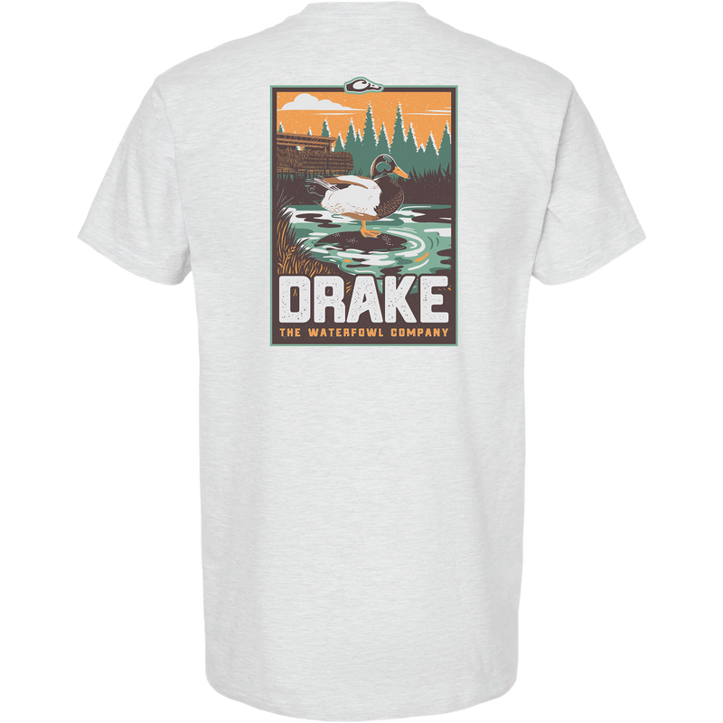 Mallard Blind Scene T-Shirt featuring a drake in a marsh with duck blind silhouette, evergreens, and orange sky. Bold DRAKE text highlights the Waterfowl Company's theme.