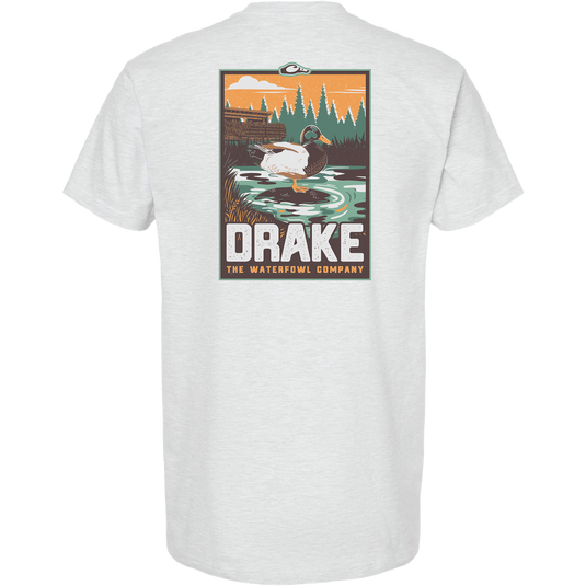 Mallard Blind Scene T-Shirt featuring a drake in a marsh with duck blind silhouette, evergreens, and orange sky. Bold DRAKE text highlights the Waterfowl Company's theme.