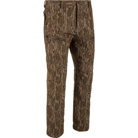 MST Youth CommandXT Softshell Pant in Mossy Oak Bottomland featuring a camouflage print, zippered hand pockets, a stretch waistband, and a button closure.