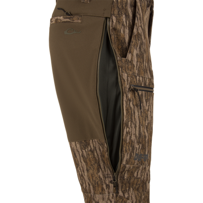 Side view of MST Youth CommandXT Softshell Pant in a brown woodland camouflage pattern, featuring an open mesh-lined thigh vent with a zipper closure.