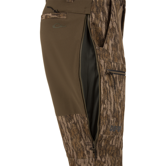 Side view of MST Youth CommandXT Softshell Pant in a brown woodland camouflage pattern, featuring an open mesh-lined thigh vent with a zipper closure.