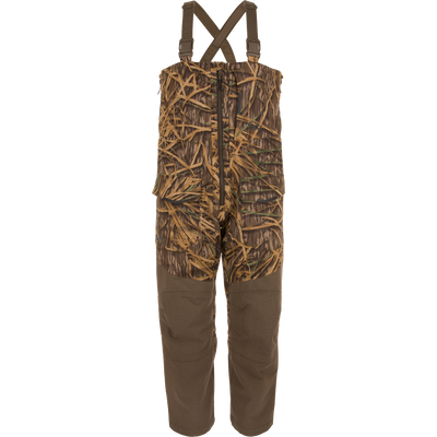 The Waterfowl LST CommandXT Bib with Primaloft in Mossy Oak Original Shadow Grass features adjustable straps, a front pocket, and PrimaLoft insulation for warmth.