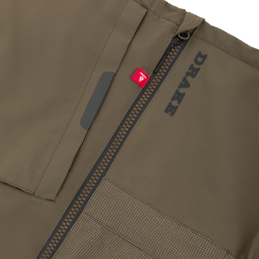 Close-up of an olive green Drake X Ducks Unlimited LST BMF Pit Bib with Primaloft, featuring a vertical zipper, a small red Primaloft tag, and black text branding.