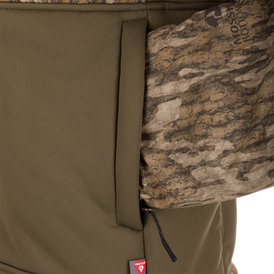 LST BMF 3-in-1 Pit Jacket with Primaloft, featuring an olive-green softshell, camo-patterned sleeve, zippered pocket, and red insulation tag near the hem.
