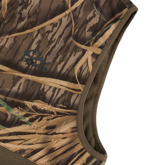 Close-up of the CommandXT Eqwader Vest by Waterfowl: a sleeveless, abrasion-resistant vest with brown/tan camo pattern, brown trim, DRAKE logo on the chest, and durable material.