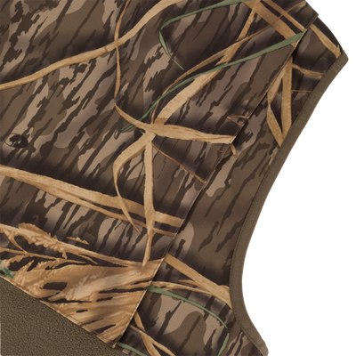 Close-up of the Waterfowl CommandXT Eqwader Vest, featuring abrasion-resistant material and a camouflage pattern in brown, tan, and green resembling grass and branches, shown on a white background.