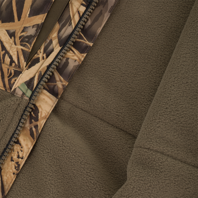 Close-up of the Waterfowl CommandXT Eqwader Vest with zipper partially open, showing soft brown fleece lining. The camo pattern features brown, green, and beige tones with leaf and grass shapes.